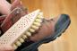 Preview: Eine Schuhschmutzbürste mit Fibre-Besatz wird zum Reinigen eines braunen Wanderschuhs verwendet. Dieser wird gerade gehalten.