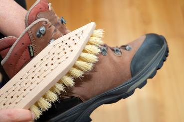 Eine Schuhschmutzbürste mit Fibre-Besatz wird zum Reinigen eines braunen Wanderschuhs verwendet. Dieser wird gerade gehalten.