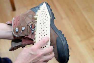 Eine Schuhschmutzbürste mit Fibre-Besatz wird zum Reinigen eines braunen Wanderschuhs verwendet. Dieser wird schräg gehalten.