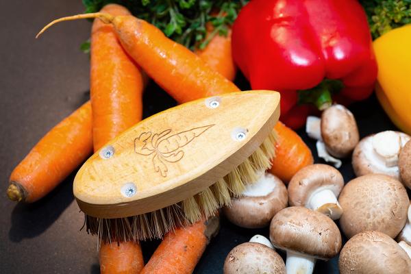 Die Gemüsebürste liegt auf ihrem Besatz. Sie liegt inmitten von Champignons, Paprika und Karotten.