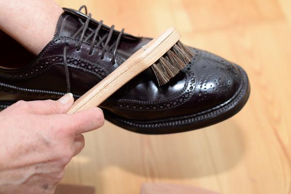 Schuhbürste mit dunklem Besatz macht einen schwarzen Schuh sauber
